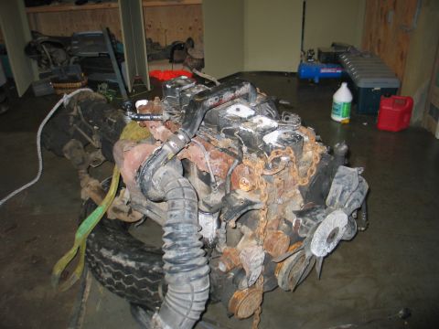 1984 Ford Bronco - Engine block with fan and hoses, appears to be heavily rusted and in need of restoration.