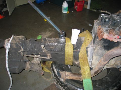 1984 Ford Bronco - Engine and transmission assembly is shown with straps and a tire, with various fluids and containers visible in the background.