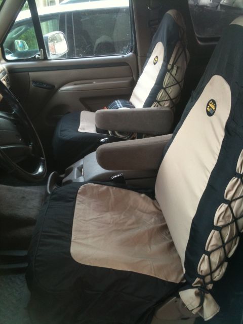 1996 Ford Bronco - The interior of an older SUV shows tan and black seat covers over the front seats, with visible armrests and a steering wheel.