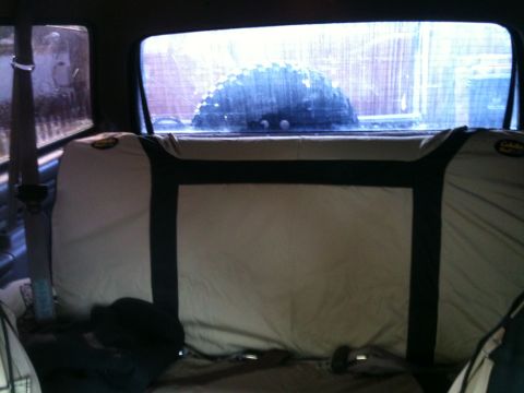 1996 Ford Bronco - The interior of a vehicle is shown, with seat covers obscuring much of the view, and a spare tire visible through the rear window.