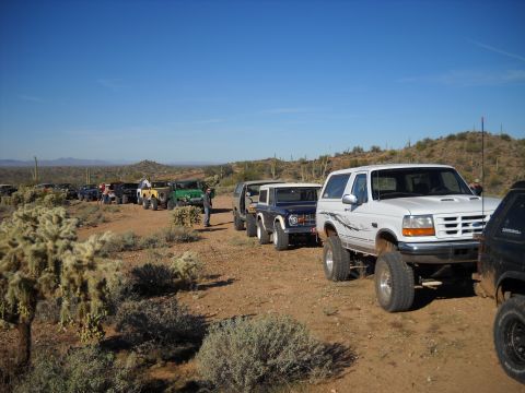 1996 Ford Bronco - Several off-road vehicles, including a 1996 Ford Bronco, are lined up on a dirt path in a desert environment.