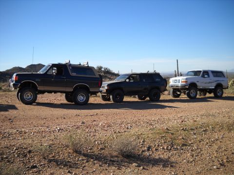 1996 Ford Bronco - Three SUVs are parked on a dirt road in a desert landscape under a clear blue sky.