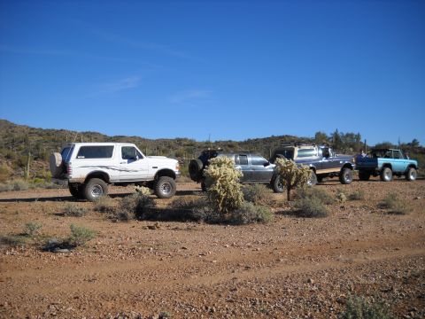 1996 Ford Bronco - A convoy of off-road vehicles, including a white Ford Bronco, navigates a dusty desert terrain under a clear blue sky.