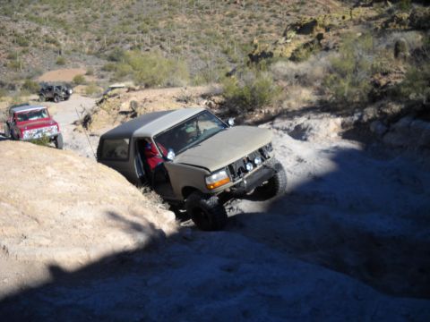 1996 Ford Bronco - A 1996 Ford Bronco tackles a challenging off-road course in a desert landscape, with other vehicles following behind.