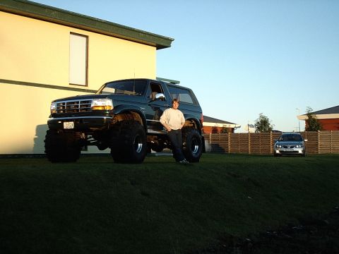 1996 Ford Bronco - A person stands next to a heavily modified 1996 Ford Bronco with oversized tires.