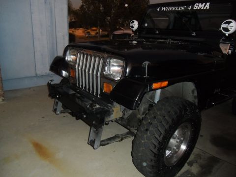 1992 Jeep Wrangler - Front view of a black 1992 Jeep Wrangler, an aftermarket bumper and large off-road tires.
