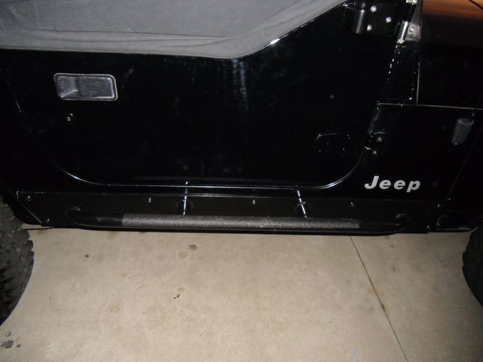 Black Jeep Wrangler door with a silver 'Jeep' decal and a black side step. The soft top is visible above the door