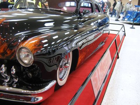 2000 Mercury Grand Marquis - A custom hot rod with a striking flame paint job and chrome accents is displayed on a red carpet.