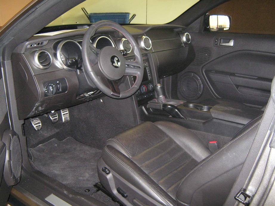 Interior shot of a car's dashboard, steering wheel, and seats. Shows a gear shifter and pedals