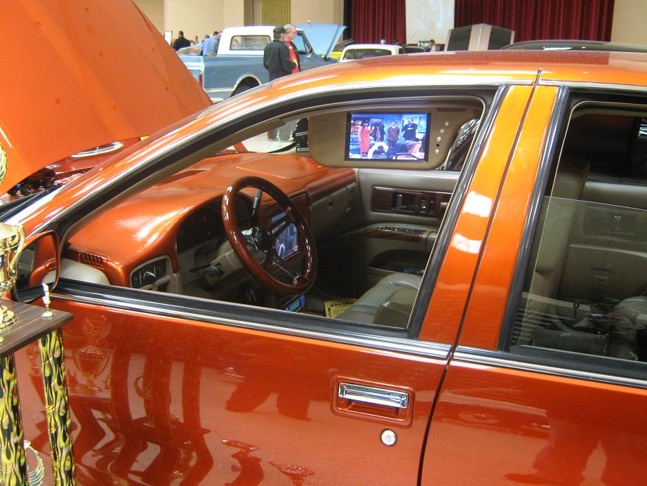 Orange car interior with wood-grain trim, a TV screen, and a trophy