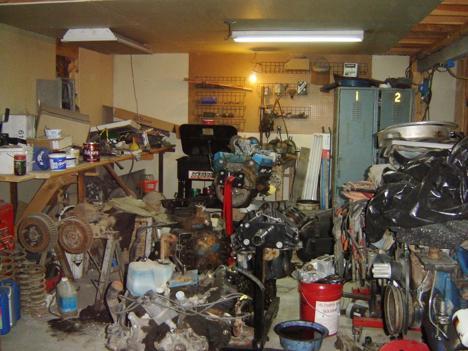 Cluttered garage interior with engines, car parts, tools, and storage cabinets