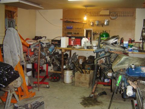1984 Ford Mustang - A cluttered garage scene with several engines and automotive parts displayed on workbenches and stands.