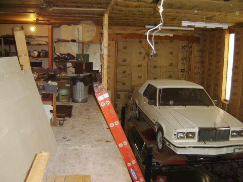 1984 Ford Mustang - A white sedan is parked inside a cluttered garage with insulation on the walls.
