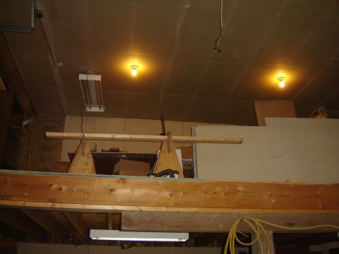 1984 Ford Mustang - The interior of a workshop or garage is shown, wooden beams, fluorescent lighting, and various construction materials.