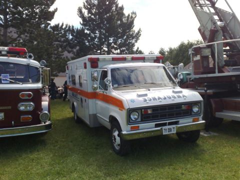 1991 Ford LTD Crown Victoria - White Ford Econoline box-type ambulance with an orange stripe and blue Star of Life, parked on grass at an emergency-vehicle show; mirror-r…