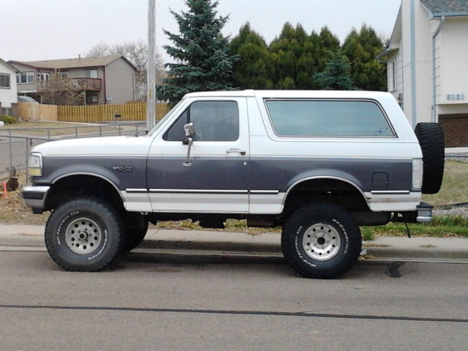 White and gray lifted Ford Bronco SUV on BFGoodrich tires, side view, parked on a residential street