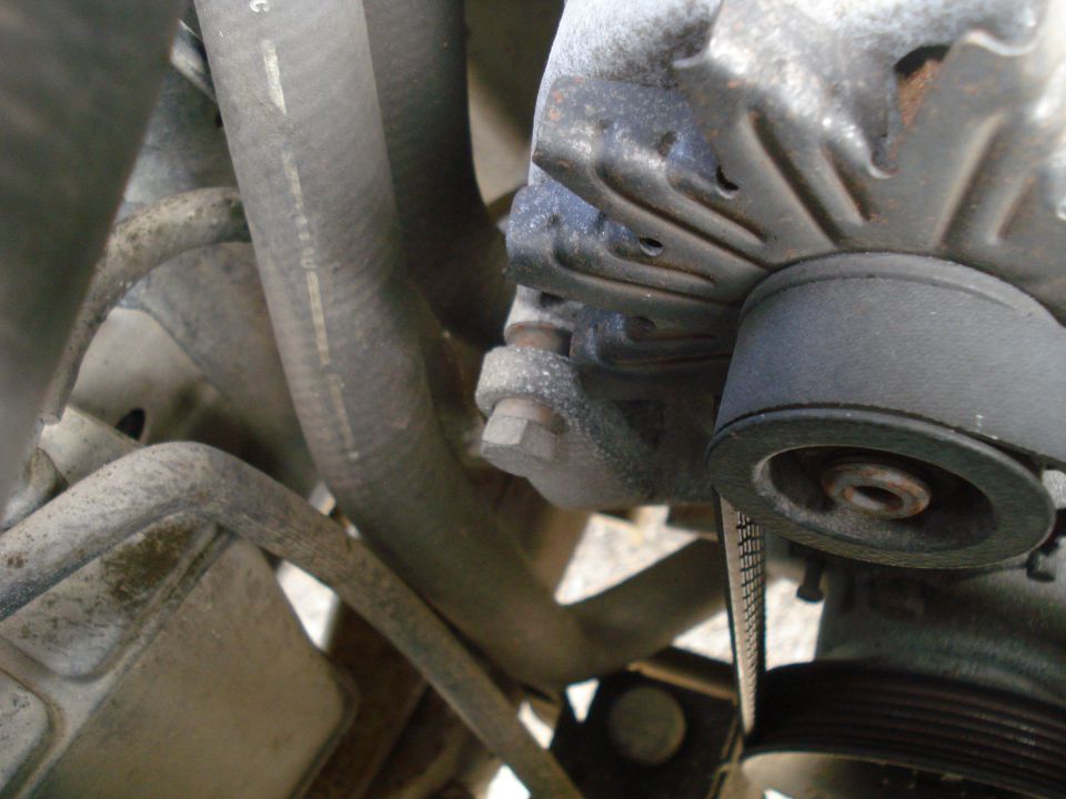Close-up of an alternator with a ribbed belt and hoses in an engine bay