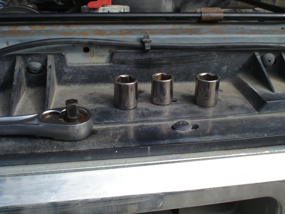 Socket wrench and three sockets on a black plastic surface, possibly in a vehicle's engine bay