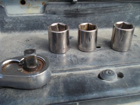 1989 Ford F-250 - A close-up view of a socket wrench and several sockets resting on a dirty surface.