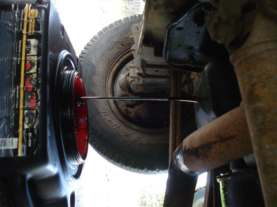 Pouring oil into a vehicle's oil pan with a tire and exhaust visible