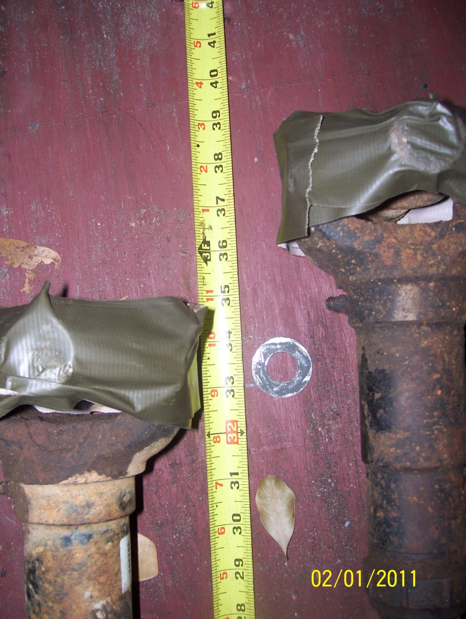 two rusty axle shafts, one with green tape, next to a tape measure showing about 35 inches