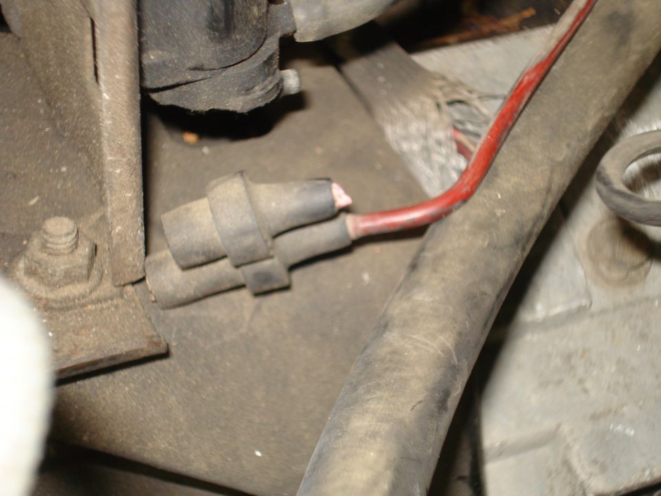 Close-up of a damaged red wire connected to a gray electrical connector in an engine bay