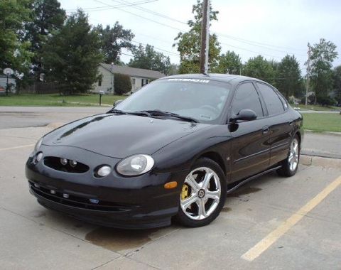 1997 Ford Taurus - Black sedan parked on concrete with a suburban house and trees in the background.