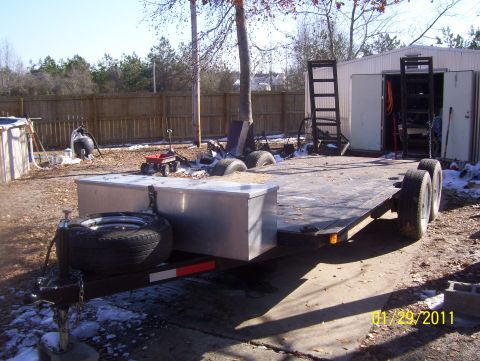 1978 Ford Bronco - Empty tandem-axle flatbed car trailer sitting on a jack in a backyard, viewed from the front-left corner with its aluminum diamond-plate to…