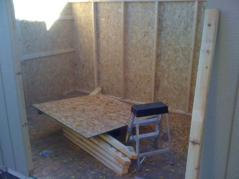 1968 Ford Mustang - The interior of a shed is shown during its construction phase, with unfinished walls and floor, stacked lumber, and a step stool.