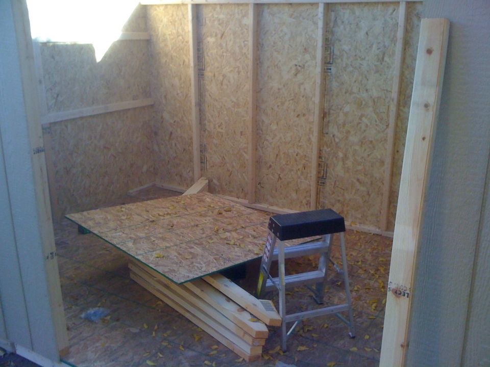 Interior of unfinished shed with plywood walls and floor, lumber, and a step stool
