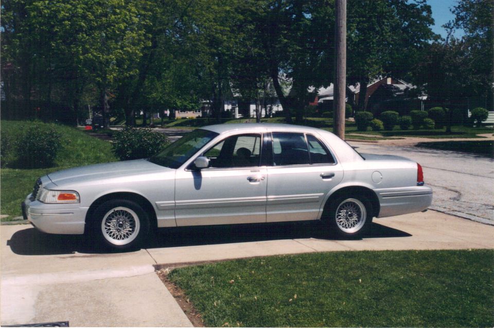 Silver full-size sedan with lace-style alloy wheels, driver-side view, parked on a sunny driveway