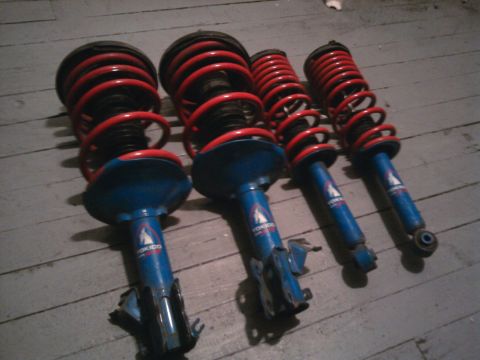 1978 Ford Bronco - Four blue and red shock absorbers are laid out on a wooden floor.