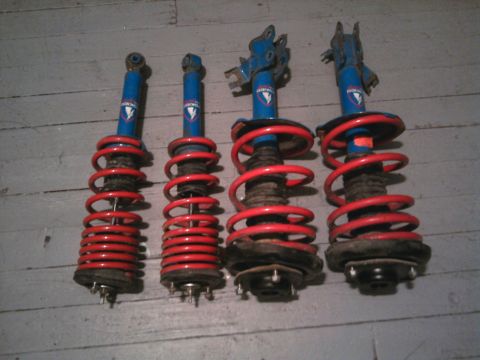 1978 Ford Bronco - A set of four suspension shock absorbers, each fitted with a red coil spring, are displayed on a floor.