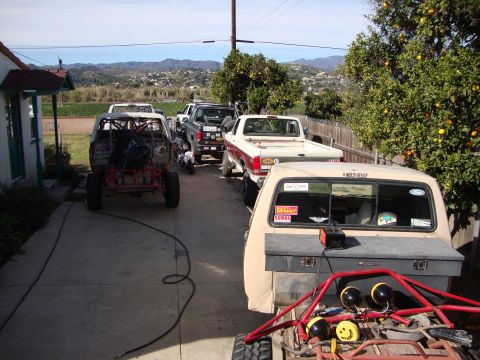 1985 Ford Bronco - A collection of trucks and off-road vehicles are parked in a driveway on a sunny day.