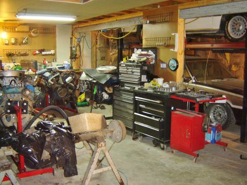 1984 Ford Mustang - A cluttered garage scene displays various car engines, tool cabinets, and a vehicle elevated on a lift.