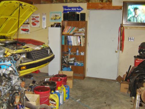 1984 Ford Mustang - A yellow car is parked in a garage with its hood open, revealing the engine compartment.