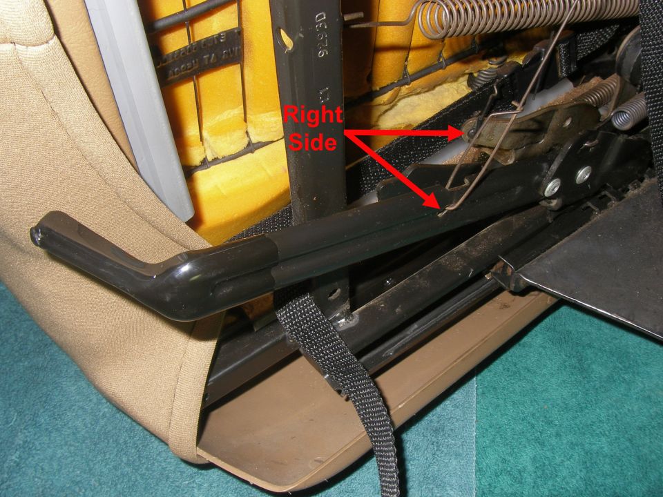 Close-up of vehicle seat mechanism, showing springs and metal components. Red arrows indicate a specific area