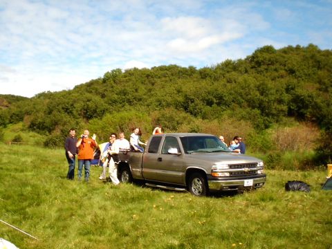 1996 Ford Bronco - A group of people gather around a gray Chevrolet pickup truck in a grassy, hilly area.