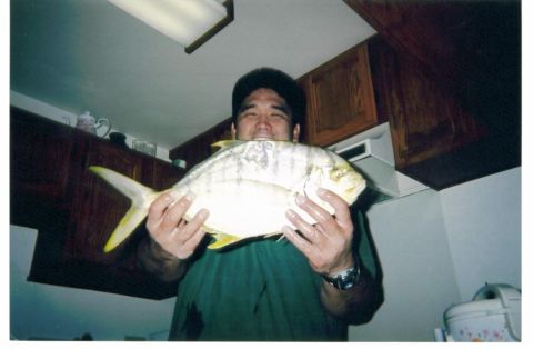 1991 Ford Bronco - A man in a green shirt stands in a kitchen holding up a large silver and yellow fish, likely a jack or pompano, with wooden cabinets and a…