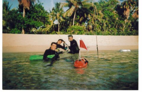 1991 Ford Bronco - Three spearfishermen in black wetsuits stand chest-deep in clear shallow water beside a red inflatable float flying a white-striped dive fl…