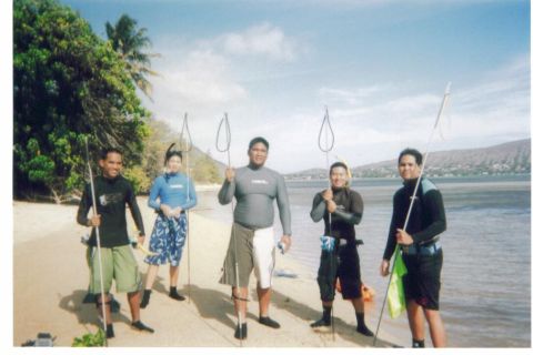 1991 Ford Bronco - Five spearfishermen in rash guards and wetsuits stand on a sandy tropical shoreline holding pole spears and Hawaiian slings, with palms and…