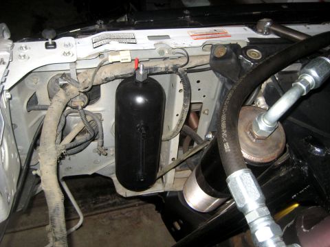 1996 Ford Bronco - Detail of a black cylindrical reservoir or accumulator mounted to a white radiator support, with a red-capped fitting on top and rubber-wra…