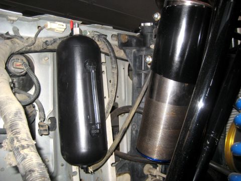 1996 Ford Bronco - Close-up view of engine bay components, including a black fluid reservoir and a metallic cylinder with visible threading.