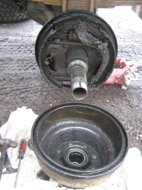 1972 Ford F-250 - A disassembled brake drum and hub assembly sits on a wet surface next to tools and a jack.