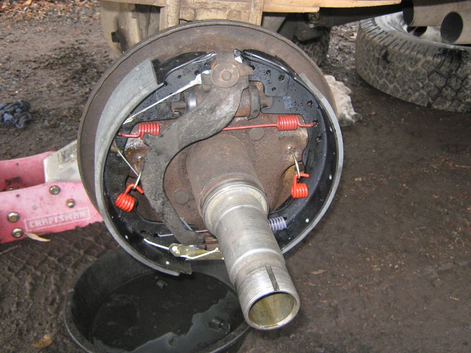 Close-up of a drum brake assembly with new red springs and brake shoes. A Craftsman jack is visible to the left