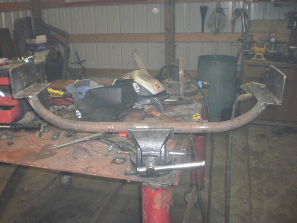 Custom trailer hitch receiver clamped in a vise on a workbench, with welding equipment nearby