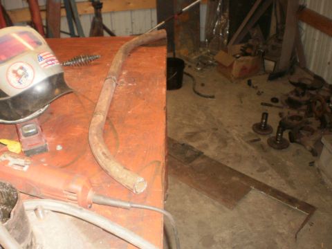 1995 Ford Bronco - A workbench with welding gear and a metal pipe, with disassembled vehicle components visible on the garage floor.