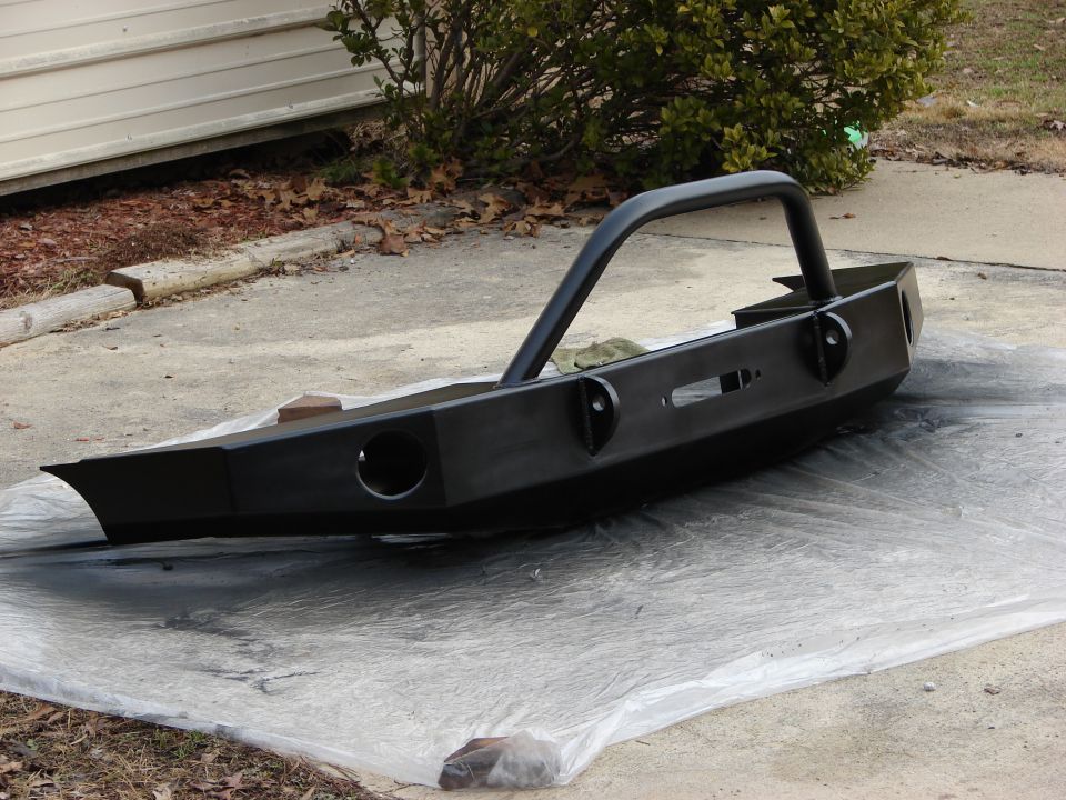 Black aftermarket front bumper with integrated brush guard, resting on plastic sheeting