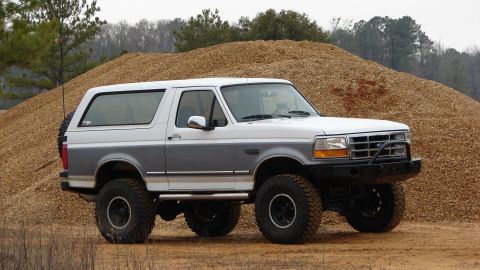 1995 Ford Bronco - This lifted Ford Bronco sits ready for adventure, its two-tone paint and stance evident against the backdrop of a large wood chip mound.