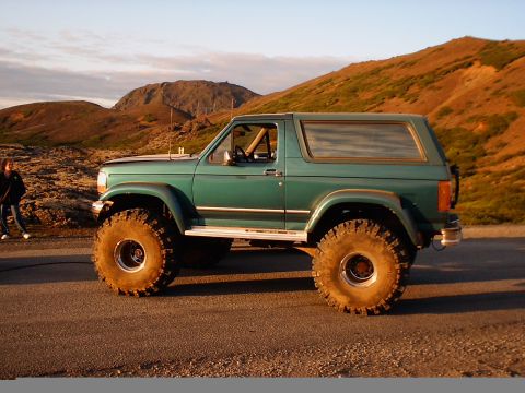1996 Ford Bronco - A modified green Ford Bronco sits on a road with a mountainous landscape in the background during sunset.